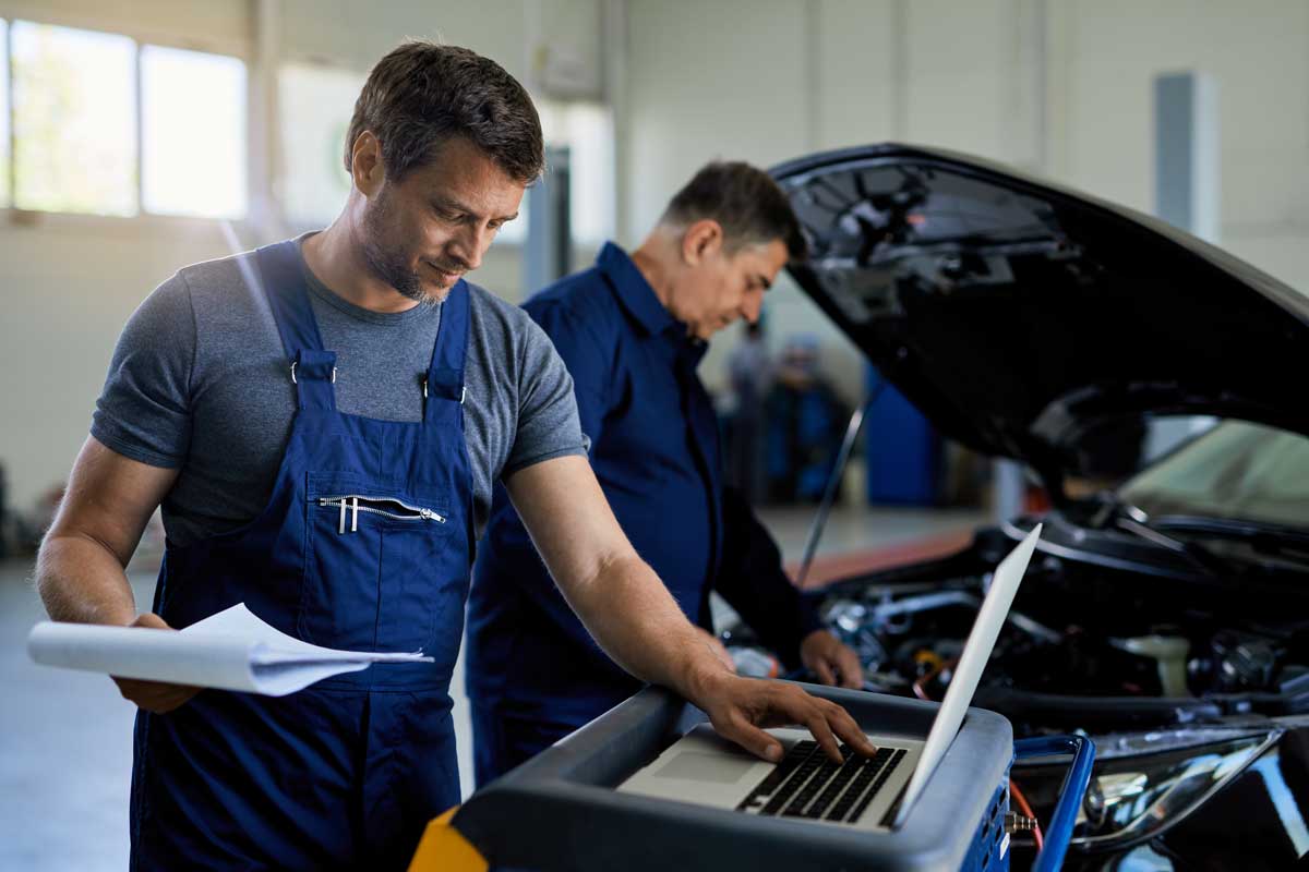 automotive quality control inspection engineer in garage viewing inspection report on laptop